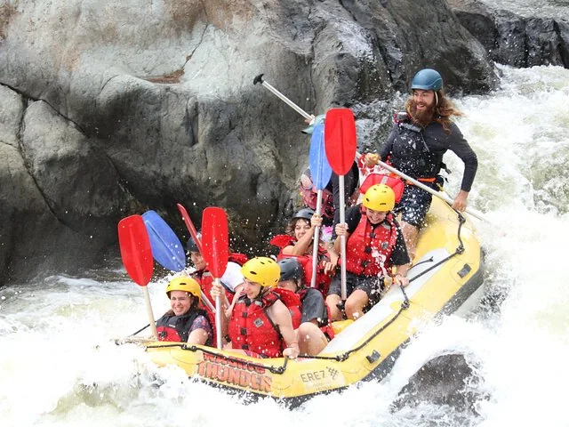 Ein gelbes Raft voller Menschen mit roten und blauen Paddeln, das durch intensive Stromschnellen spritzt.