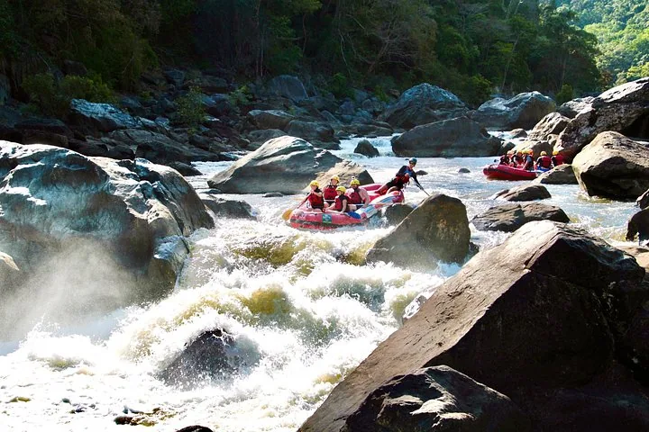 Ein gelbes Raft manövriert zwischen großen, glatten grauen Felsen in den Stromschnellen des Tully River.