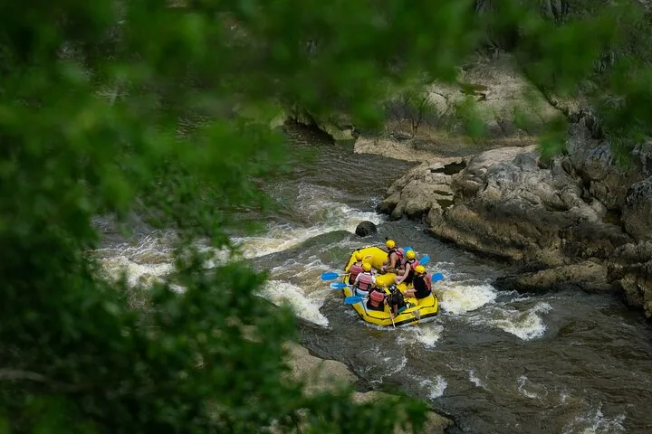 Luftaufnahme durch Bäume auf ein gelbes Raft, das milde Stromschnellen zwischen Felsen bewältigt.