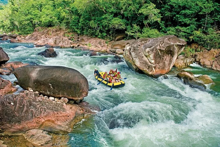 Ein Raft beim Bewältigen von Stromschnellen am Tully River, umgeben von großen Felsbrocken und üppiger Vegetation.